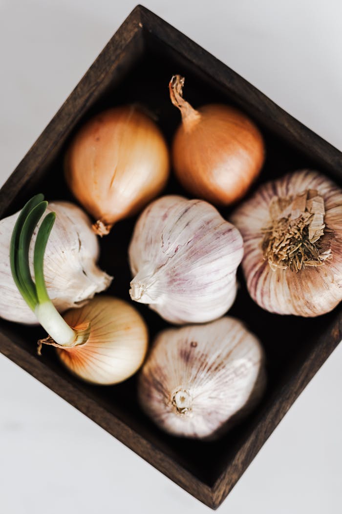 Top view of fresh garlic and onions arranged in a rustic wooden box, perfect for culinary themes.